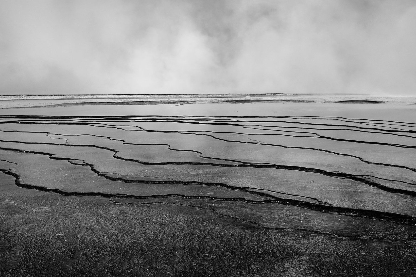 Black and white steam rolling over terraced mineral pools with dark ridged edges.
