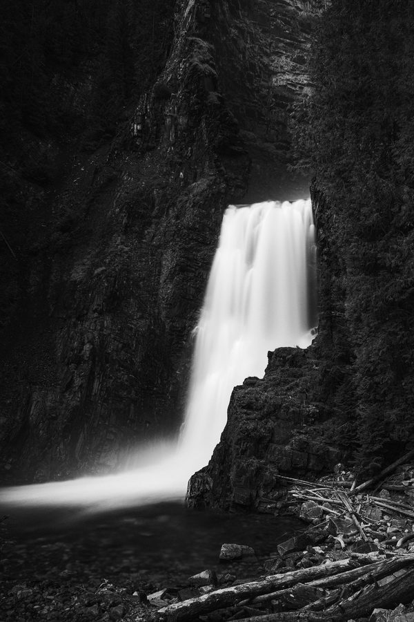 Black and white long exposure waterfall in a dark gorge beside a rock cliff.