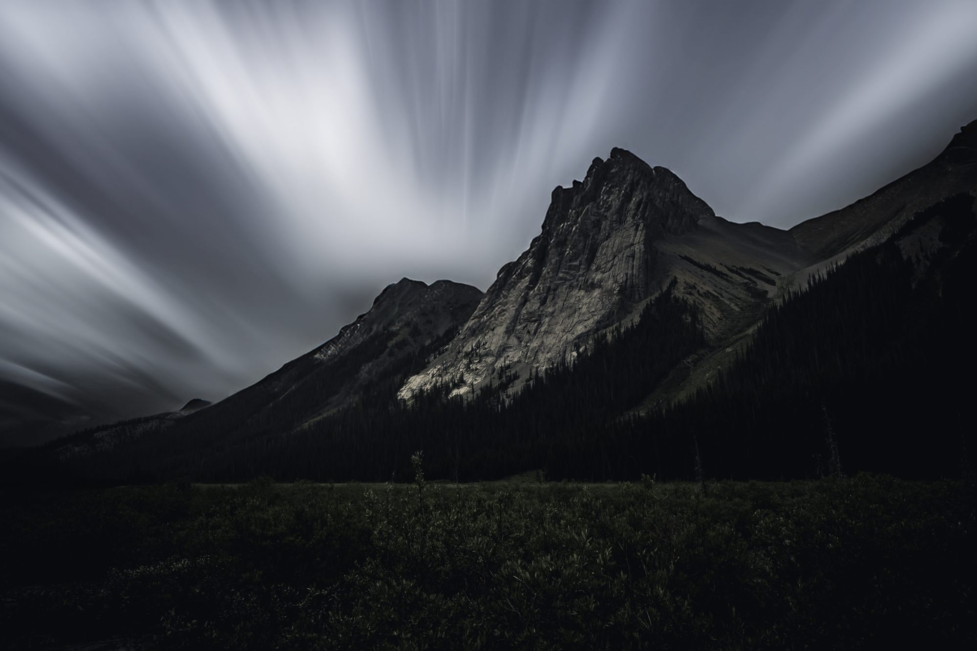 Long exposure clouds streaking across the sky above a jagged dark peak.